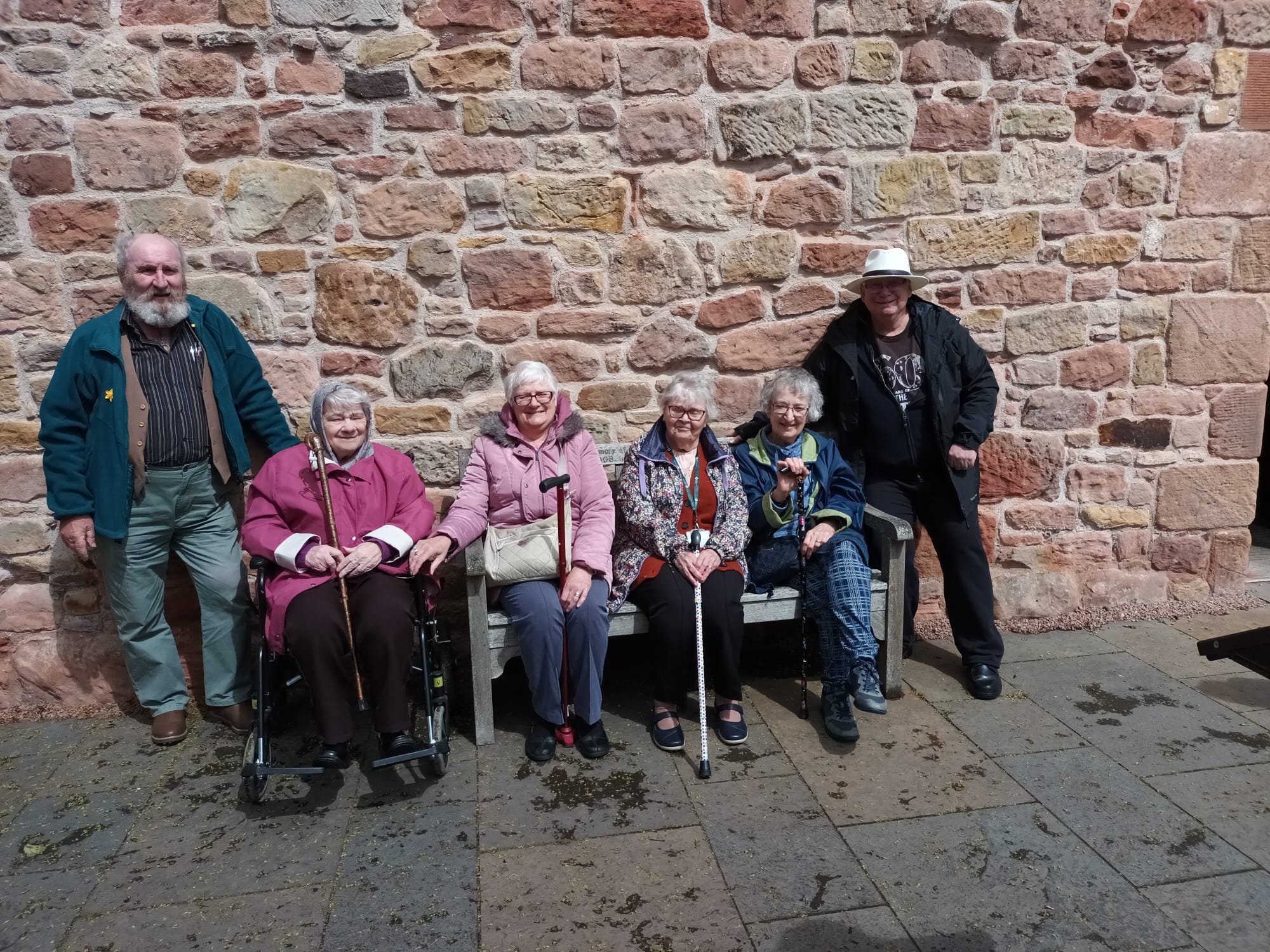 A picture of elderly from St David's Bradbury Day Centre in Midlothian, on a social excursion sat in front of a stone wall